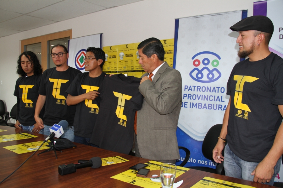 En reconocimiento a su apoyo, los representantes de los colectivos culturales entregan la camiseta promocional del concierto al prefecto de Imbabura, Pablo Jurado. 